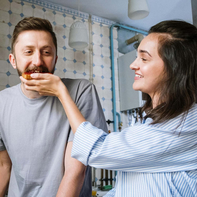 Woman feeding a man a slice of toast in a kitchen