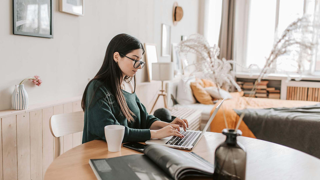 woman sitting at a table with an open book typing on a laptop