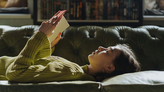 woman in green long sleeve shirt lying on couch reading a book