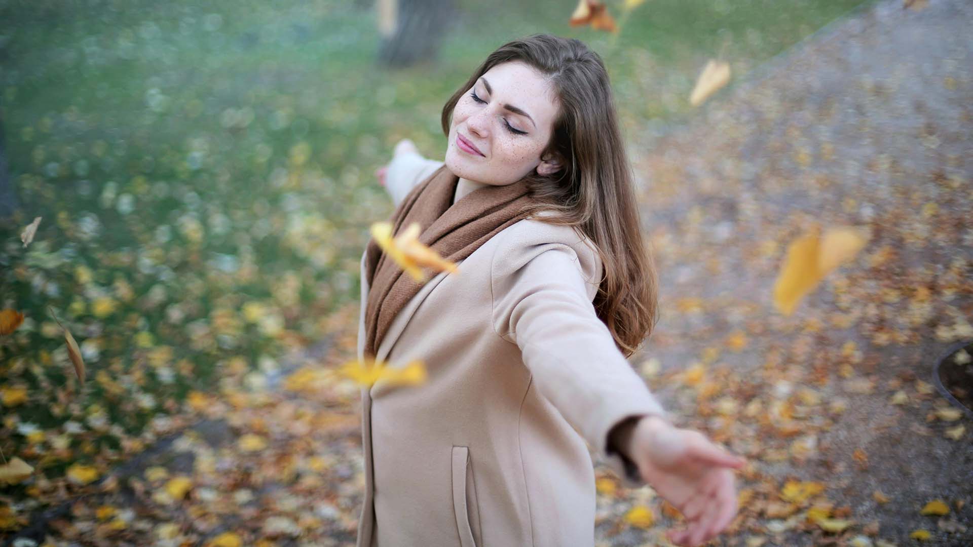 woman in brown coat with leaves falling