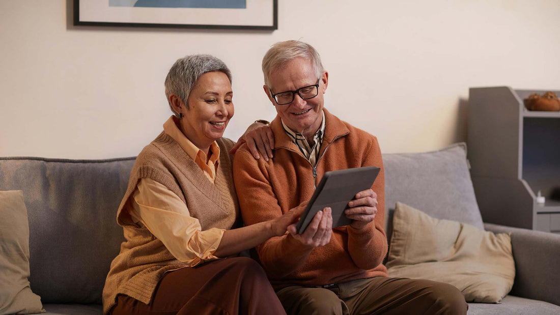 Two older adults sitting on a couch looking at a tablet