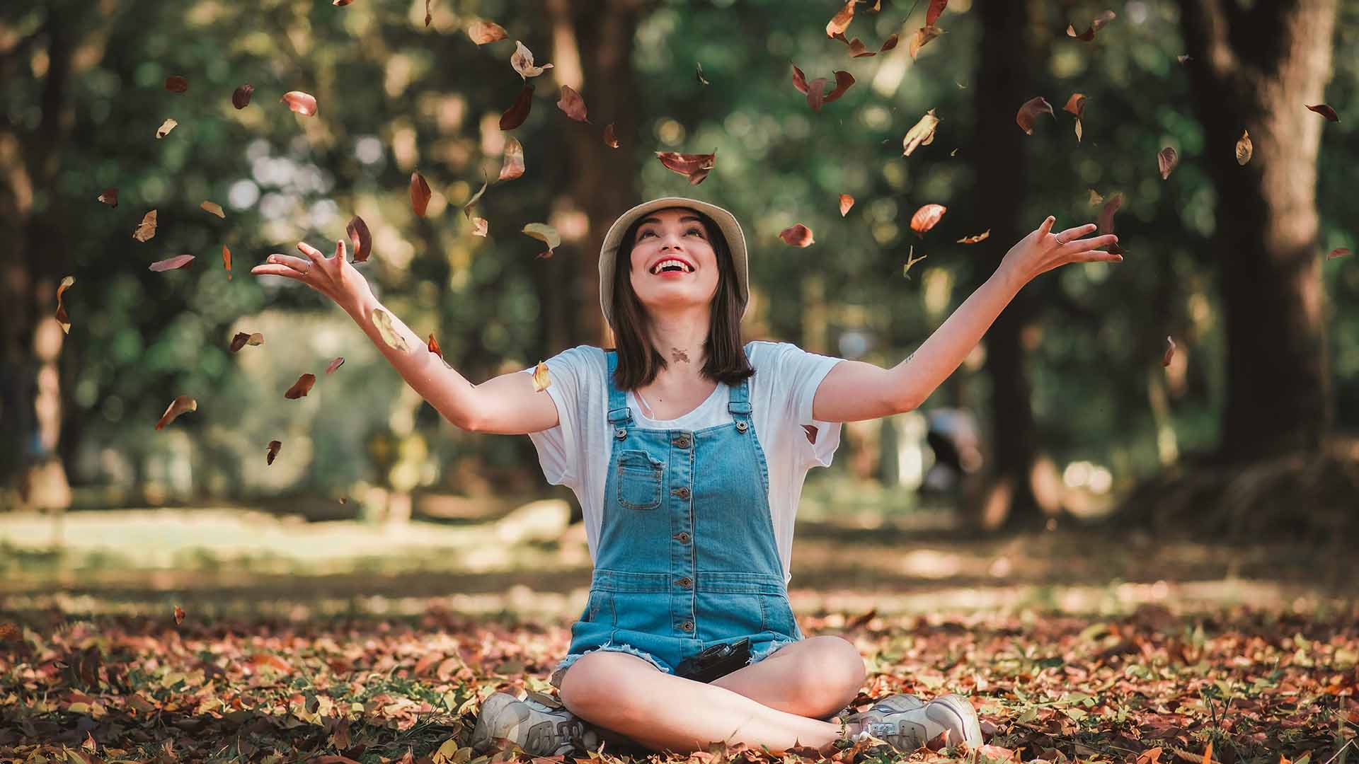 woman sitting outside smiling and tossing leaves in the air