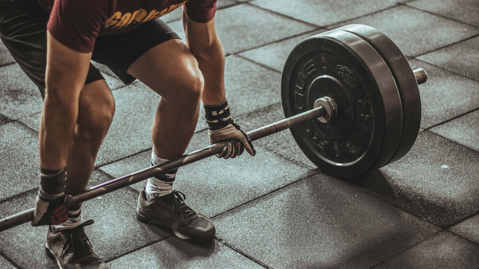 Person bending to lift a barbell off a gym floor