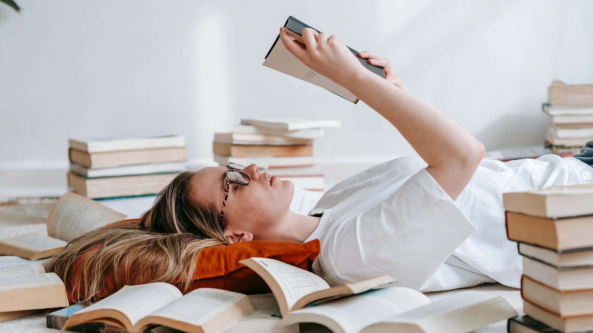 Woman reading on her back among stacks of books