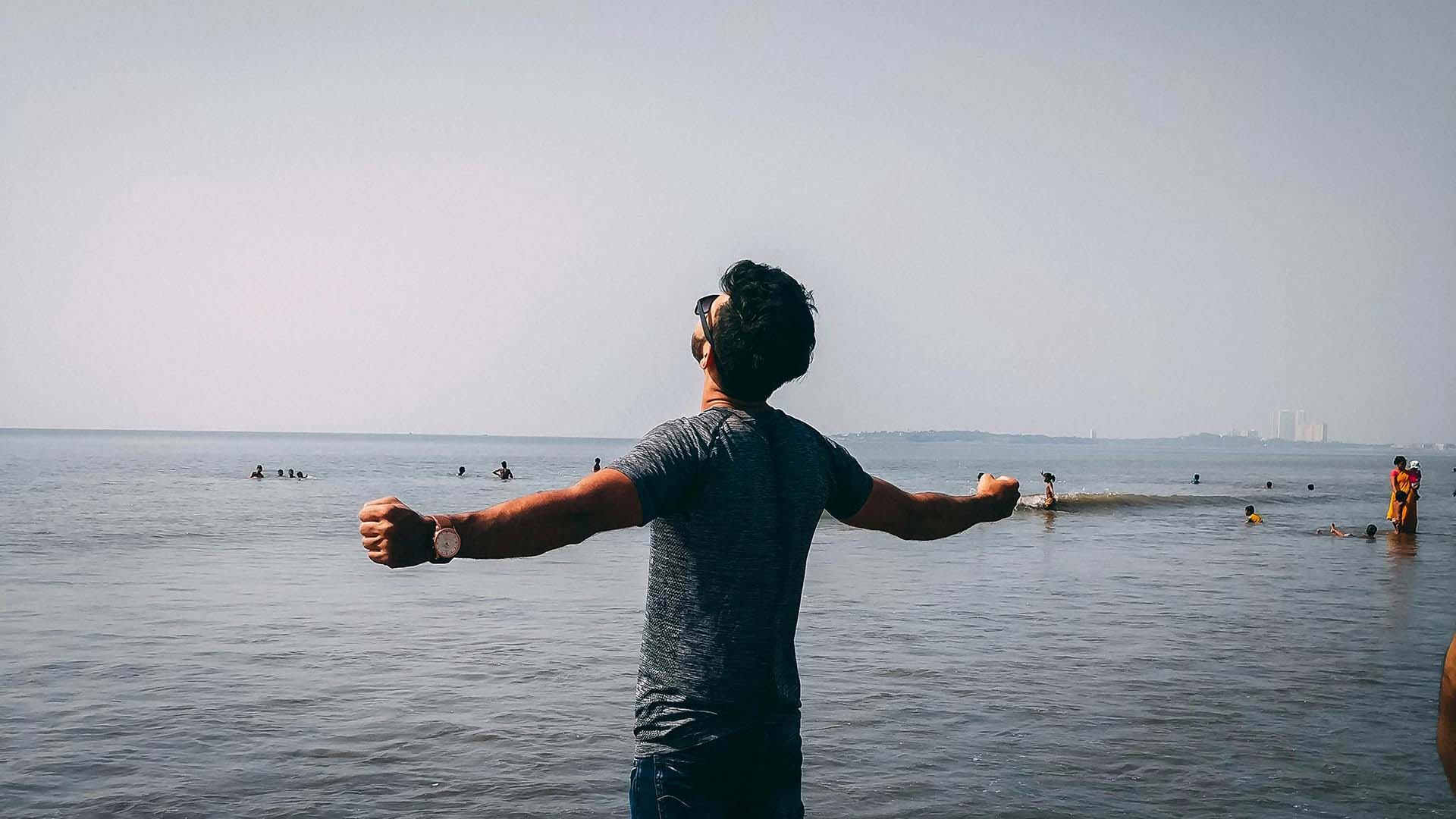 guy standing on a beach looking at the ocean with arms outstretched