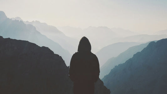 silhouette of a man in hoodie standing and looking at the mountain