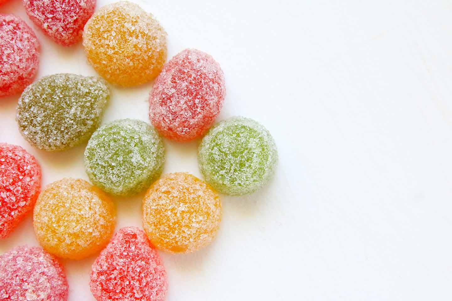 Red, green, and orange gummy candies with a sugar coating on a white background.