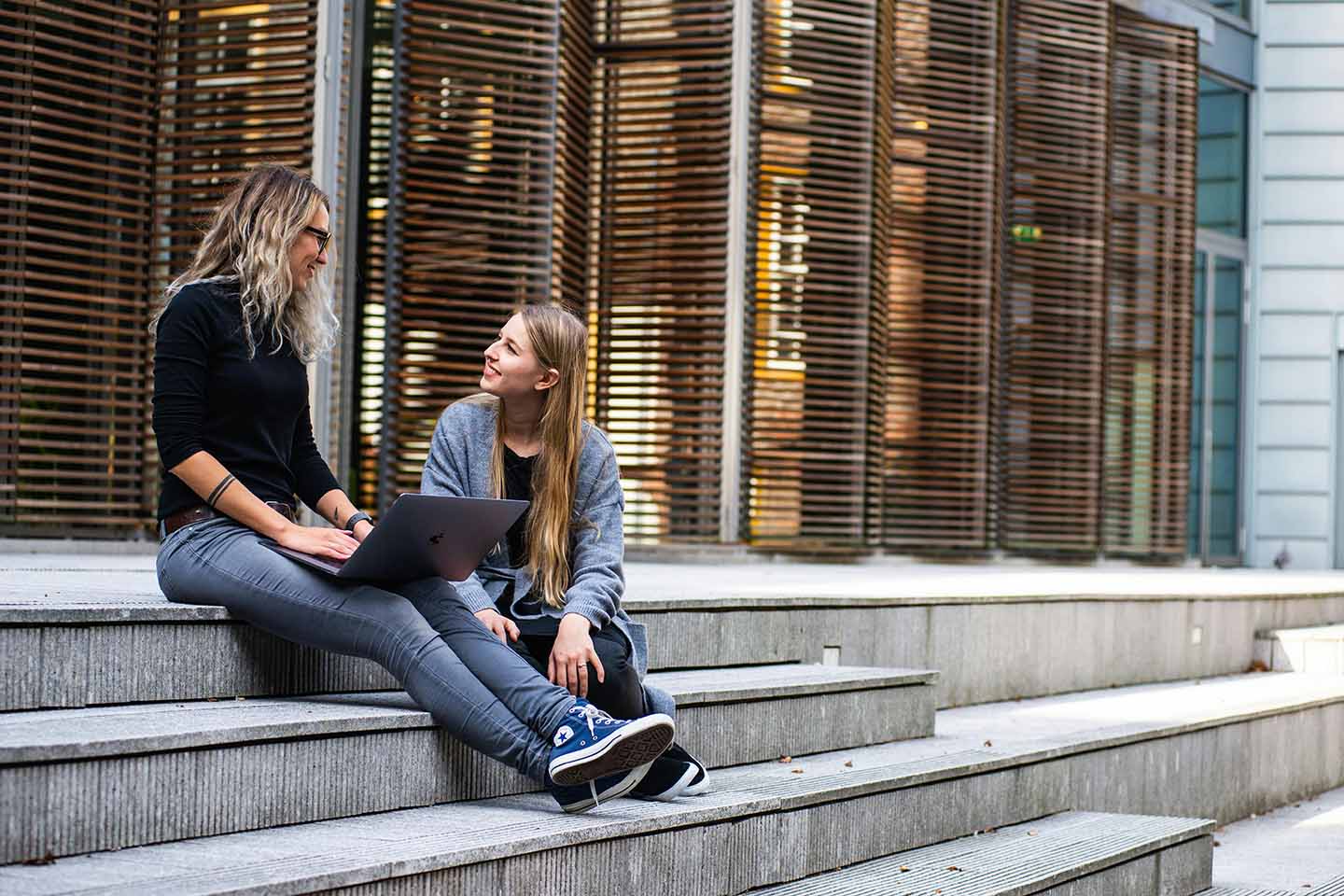 two women sitting on stairs and talking with laptop