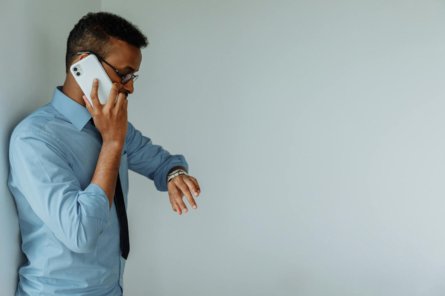 man in blue shirt talking on the phone and looking at his watch