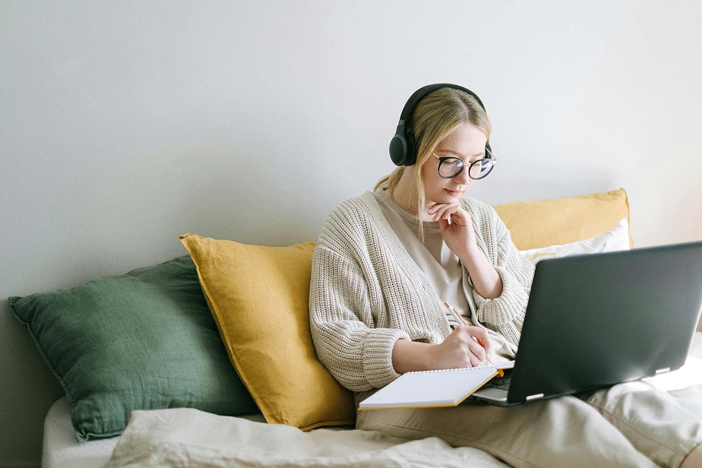 woman sitting on couch looking at laptop and writing in notebook