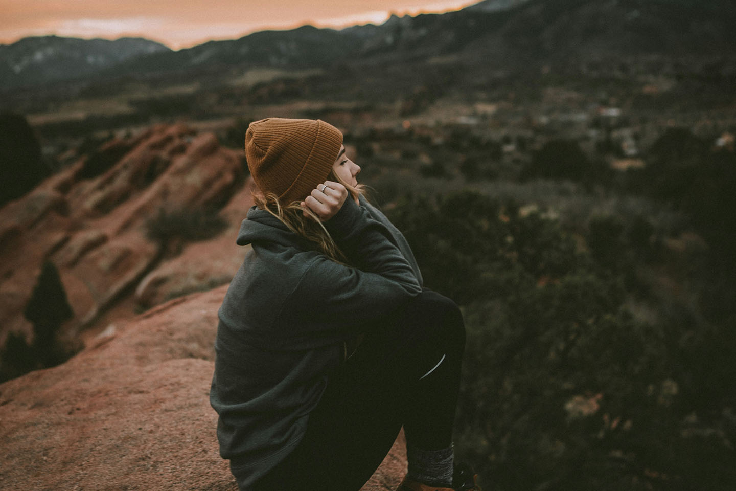 woman in a hat and jacket sitting on a rock on a cloudy day