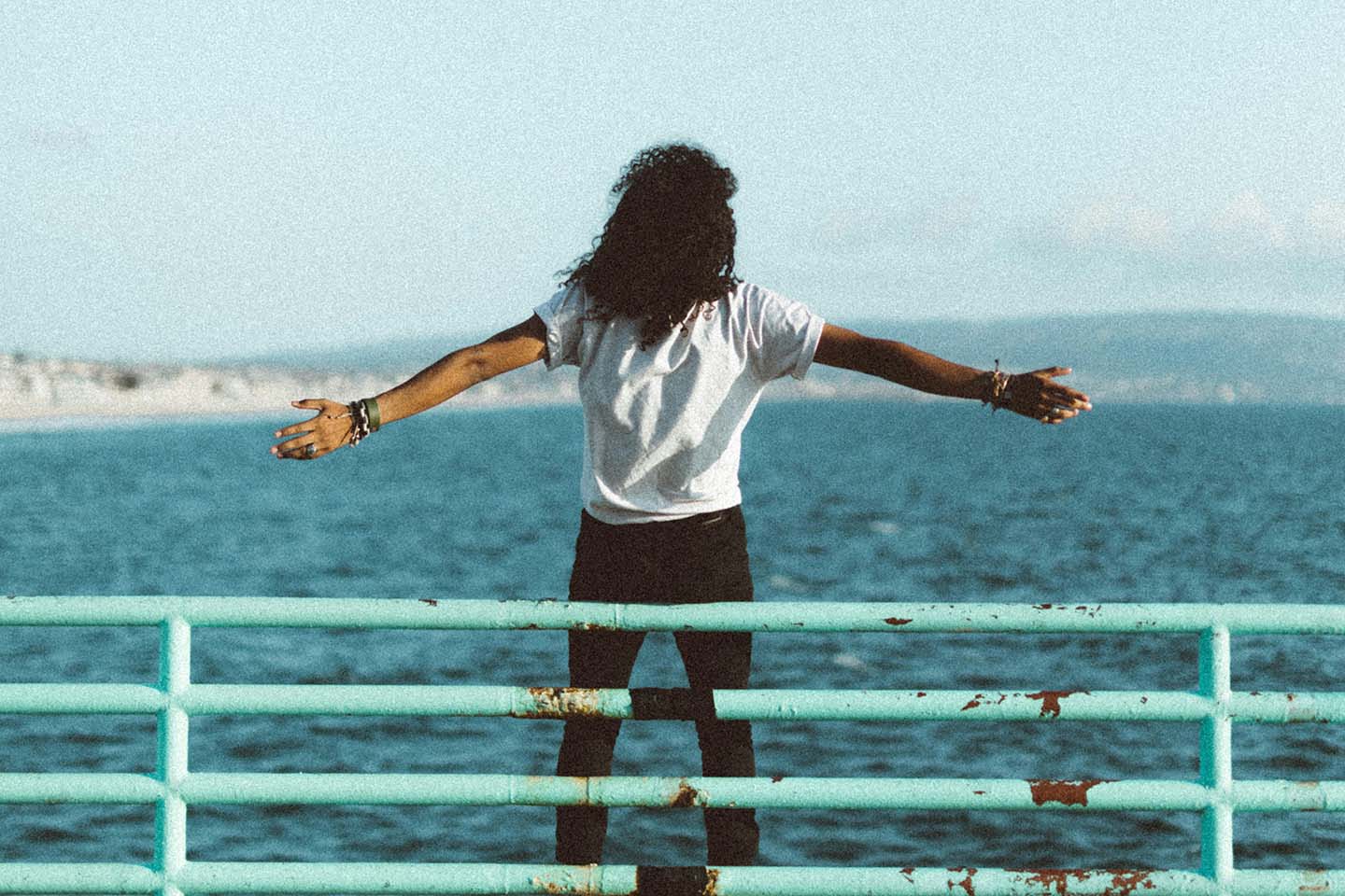 person standing in front of a railing looking at the ocean with arms outstretched