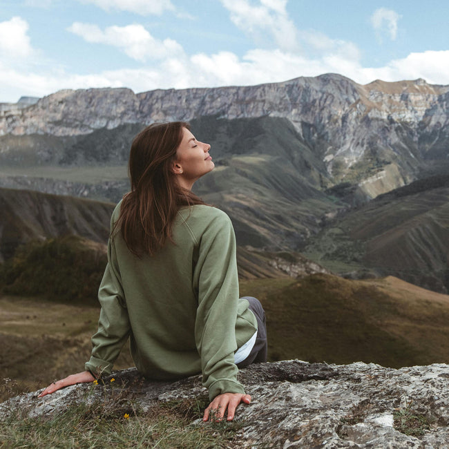 woman sitting outside on a rock smiling while looking at mountain range